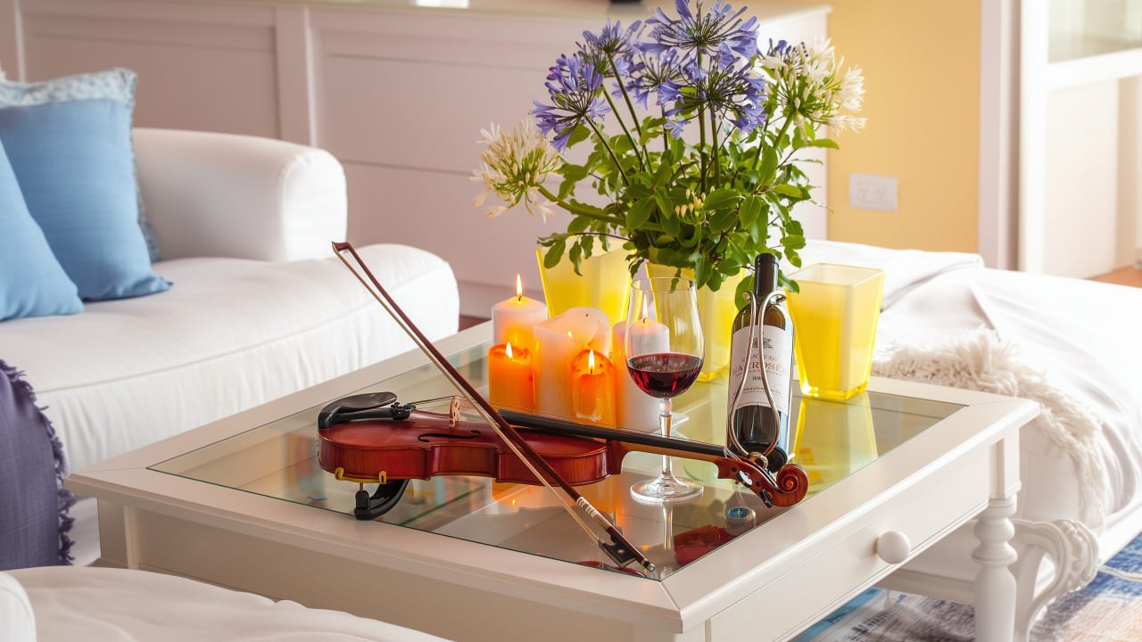 A violin and bow on a glass coffee table with lit candles, red wine and purple agapanthus flowers at Bay House.