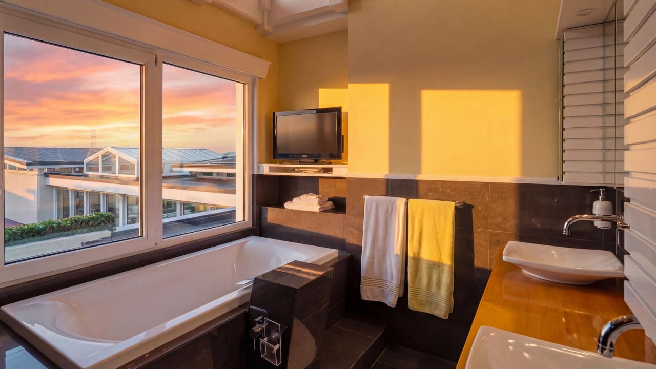 Annex master ensuite with built-in soaking bath, wall-mounted TV and large sunset-view window at Bay House.