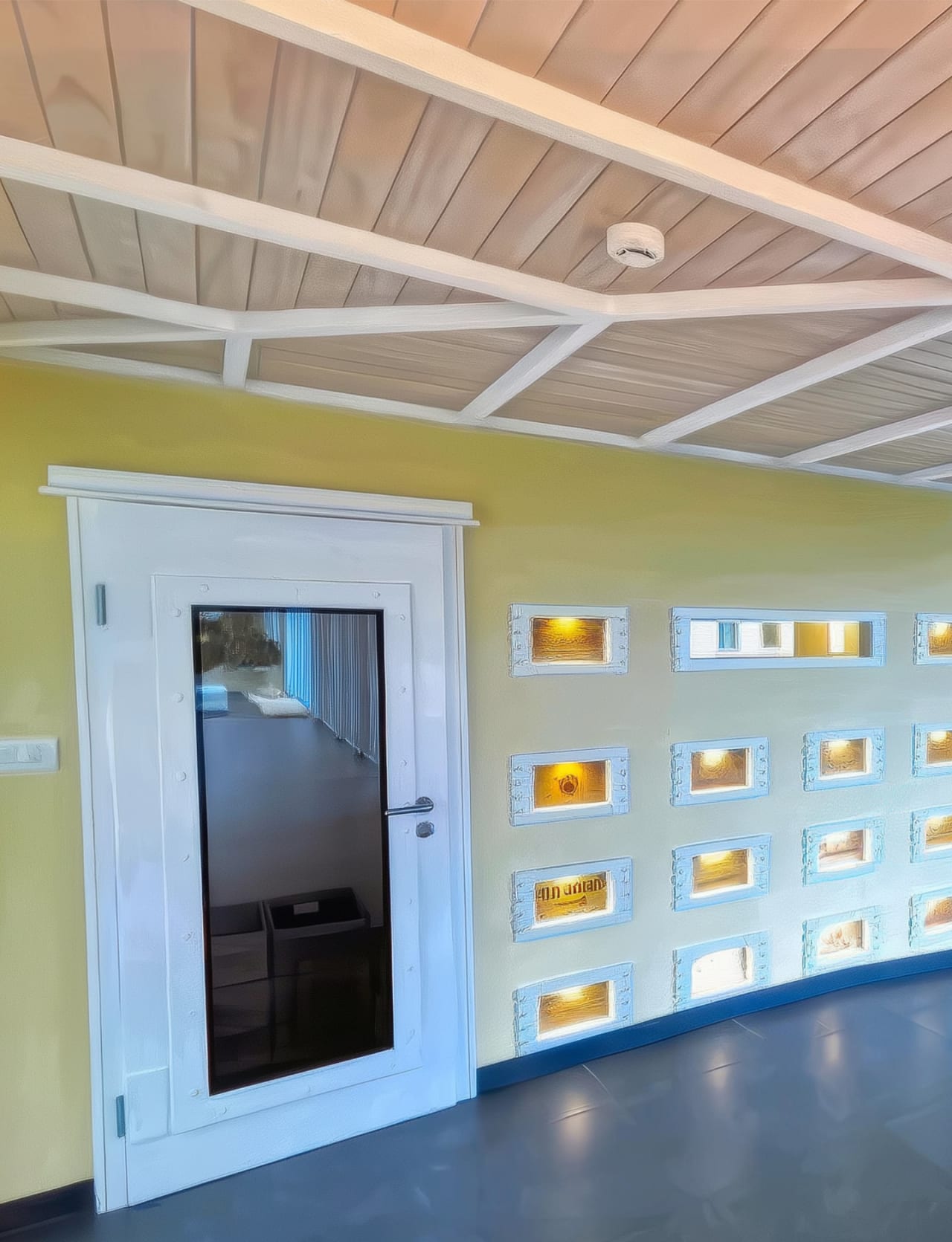 Portrait of Bay House entrance doorway and backlit wine case display niches with warm amber uplight on dark polished floor.