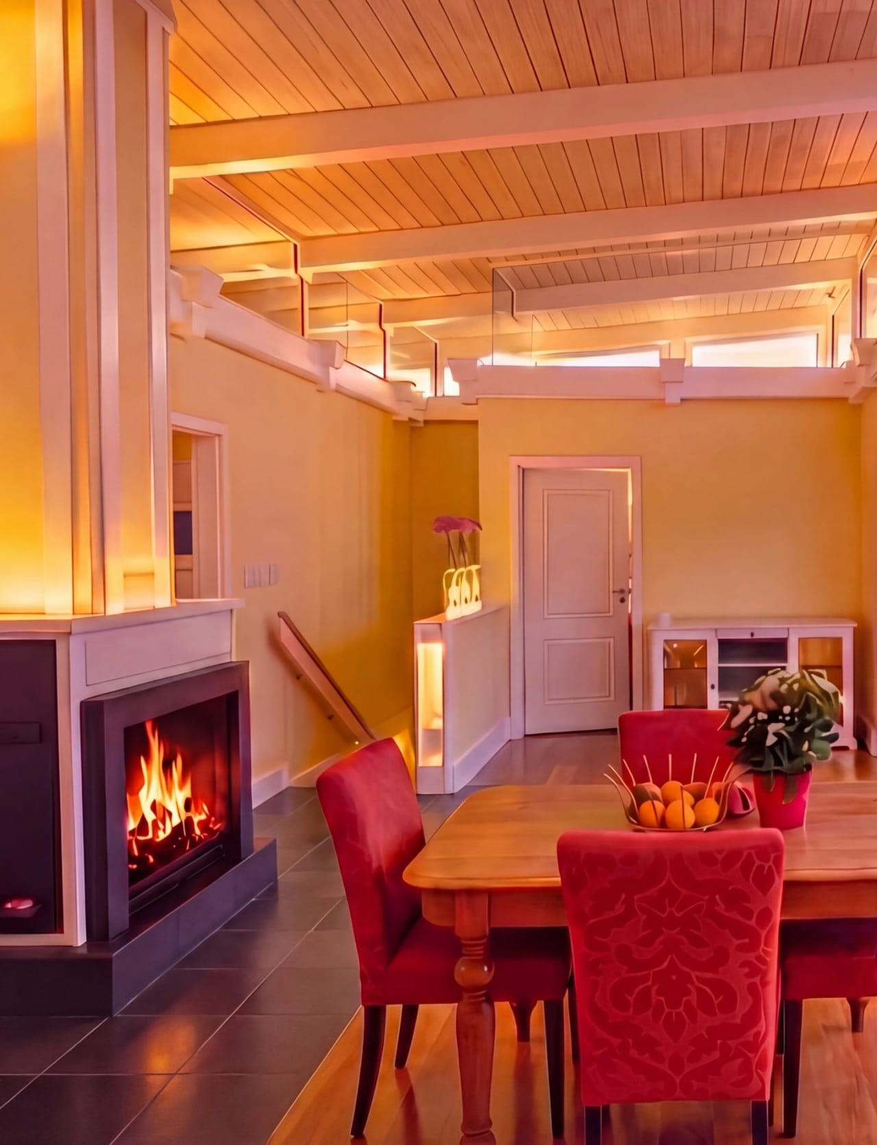 Annex dining — open fireplace burning, red chairs, T&G pine ceiling above, stairs beyond, luxury NZ coastal guest house