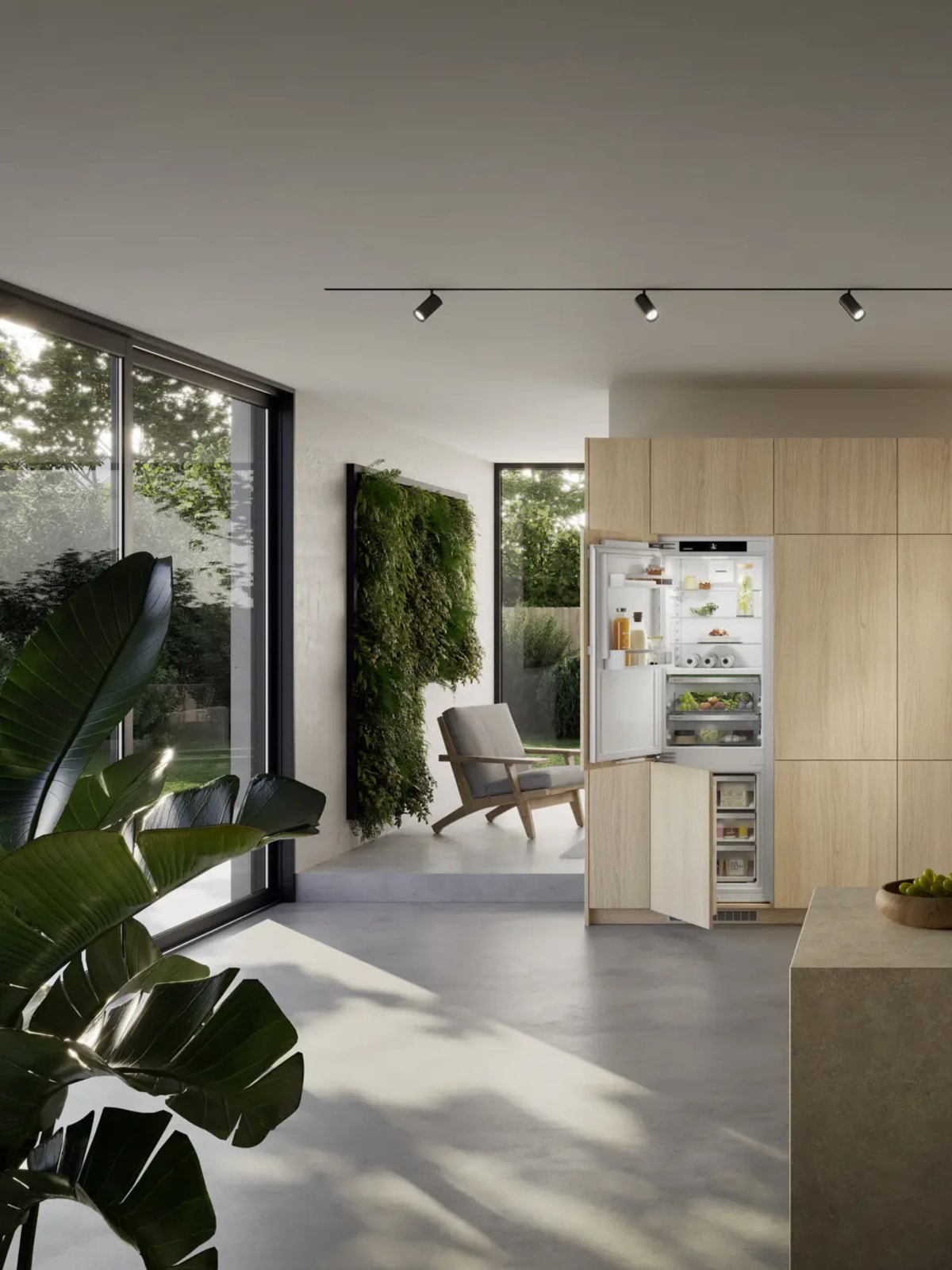 Colonne en chêne clair avec réfrigérateur-congélateur Liebherr intégré ouvert, îlot en pierre au premier plan