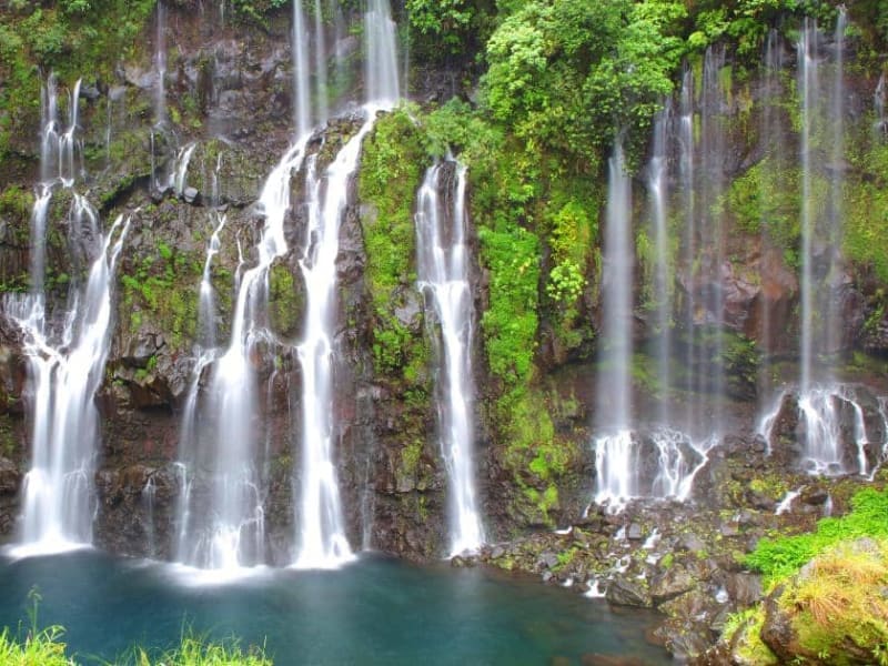 Dizaines de filets d'eau de la cascade Grand Galet tombant dans un bassin bleu, parois couvertes de végétation, Langevin
