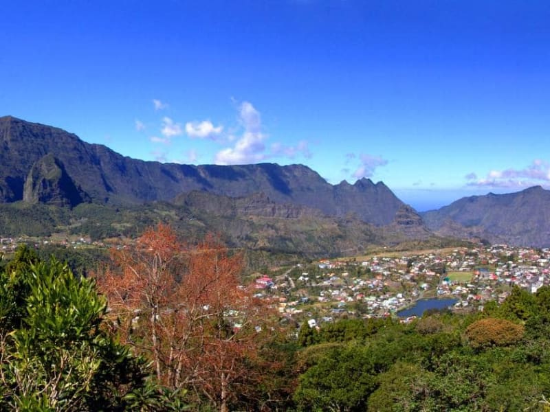 Cirque de Cilaos vu des hauteurs, village et plan d'eau au fond, arbre aux feuilles rousses au premier plan et remparts par temps clair