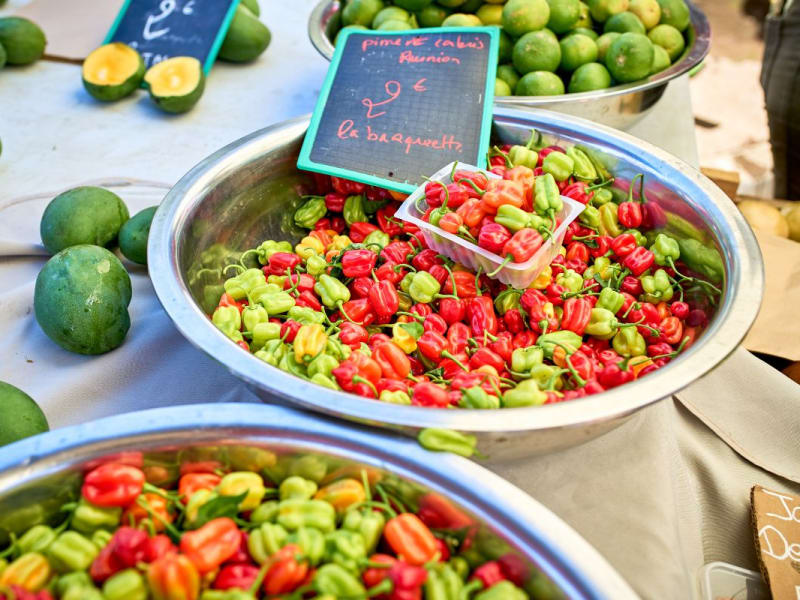 Bassine de piments rouges, jaunes et verts sur un étal de marché, ardoise « piment de Cabris Réunion, 2 € la barquette »