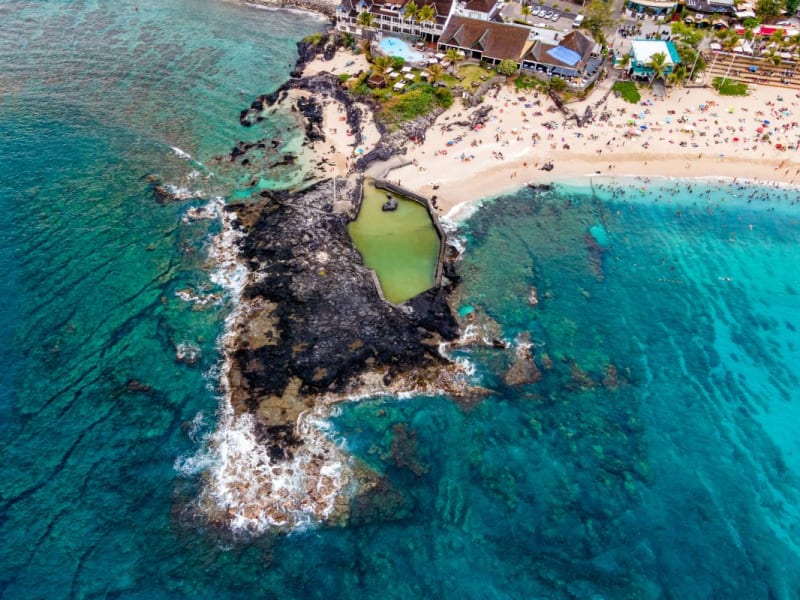 Vue aérienne de Boucan Canot, piscine naturelle creusée dans une avancée de roche noire, plage de sable clair et eau turquoise