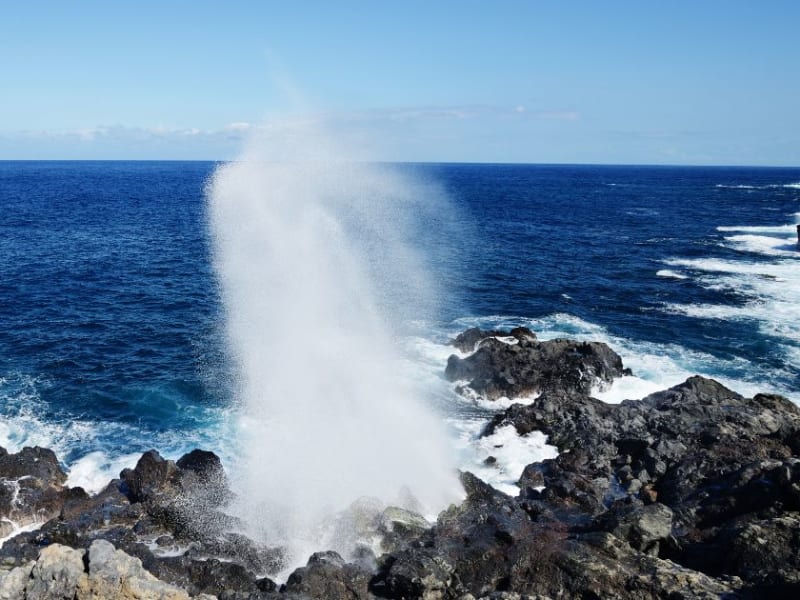 Gerbe d'eau projetée par la houle entre les roches volcaniques noires du littoral, océan bleu profond, le Souffleur