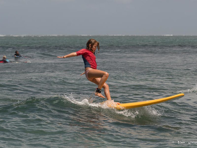Surfeuse débutante en lycra rouge sur planche de surf jaune en cours sur le spot de Saint-Leu, La Réunion