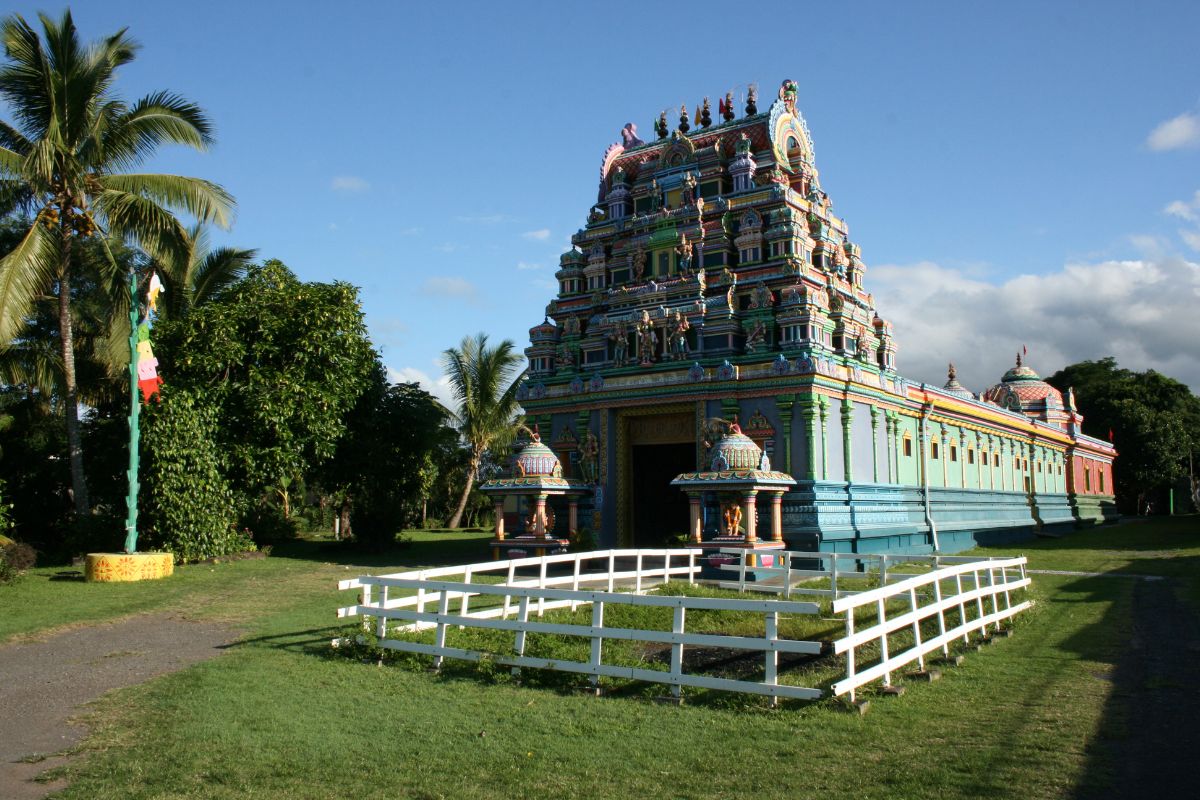 Façade complète du temple tamoul Maryen Peroumal à Saint-André : gopuram coloré, pelouse, palmiers et drapeau cérémoniel, La Réunion