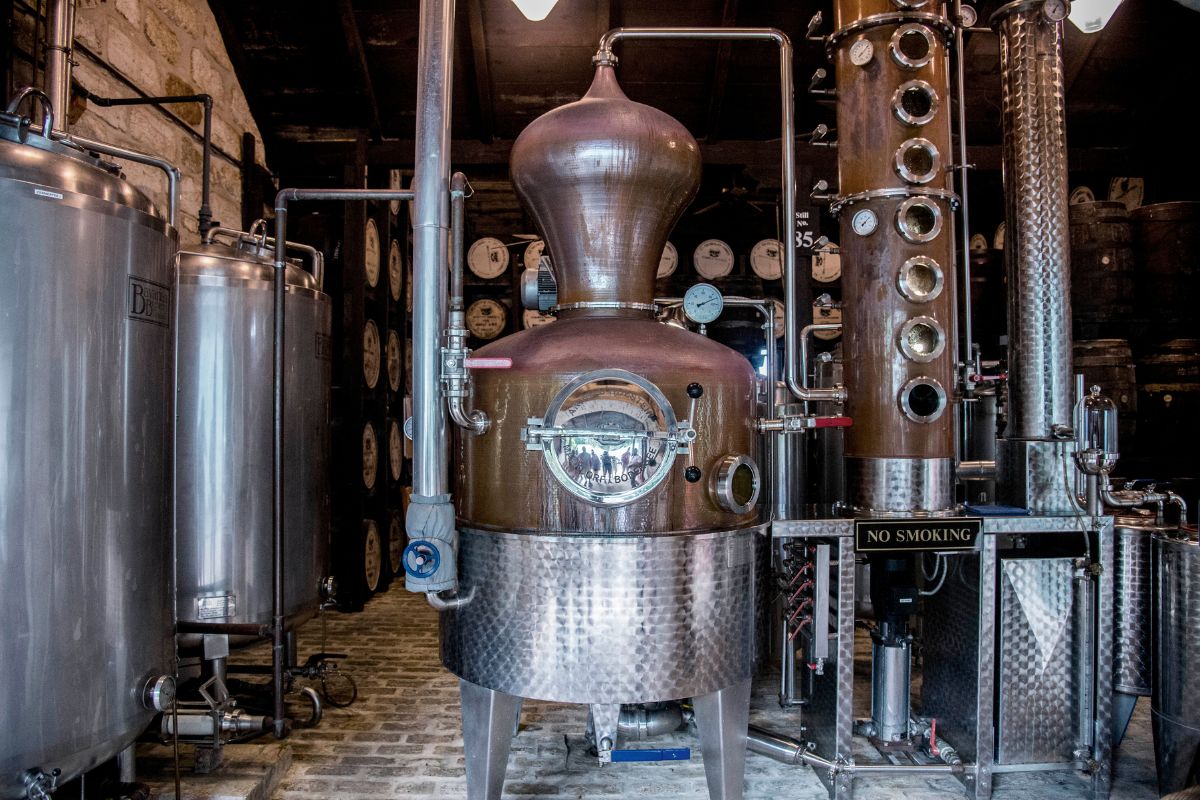 Alambic en cuivre poli et colonne de distillation, salle des chaudières d'une distillerie de rhum à La Réunion, fûts en arrière-plan