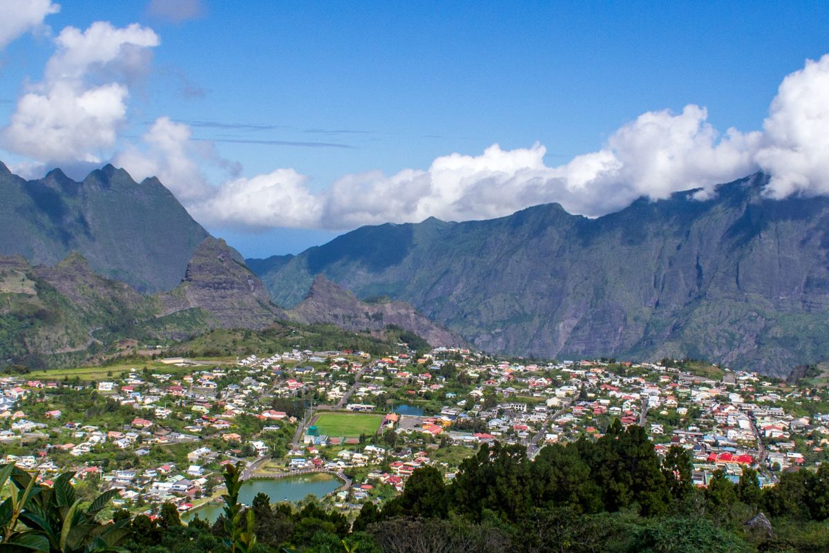 Vue aérienne du cirque de Cilaos depuis les hauteurs : village et mare à joncs au pied des remparts, route des 400 virages serpentant la montagne, La Réunion