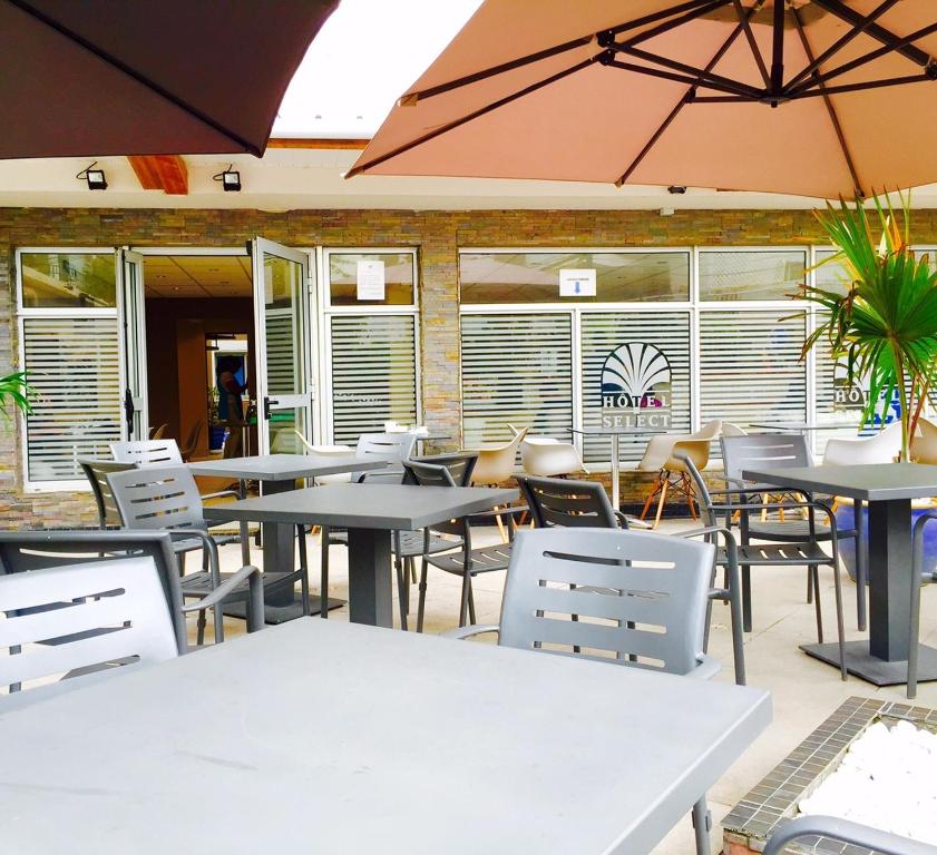 Terrasse couverte de l'Hôtel Select avec parasols, tables et façade pierre apparente affichant l'enseigne