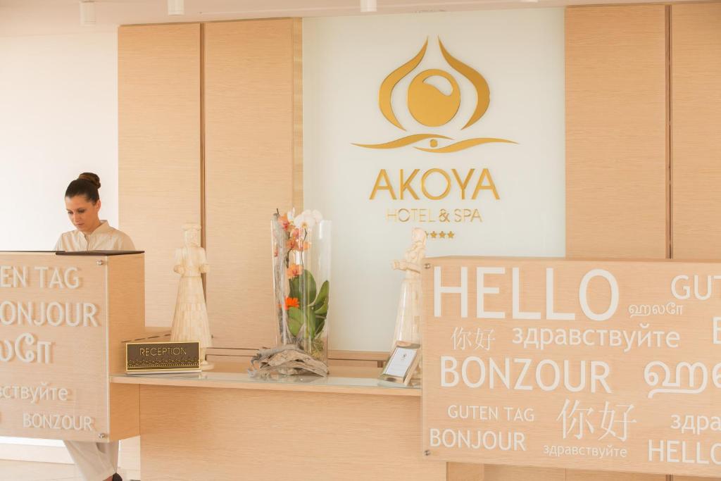 Réception de l'Akoya Hôtel & Spa avec logo doré, statues vacoa et panneaux multilingues Hello Bonzour