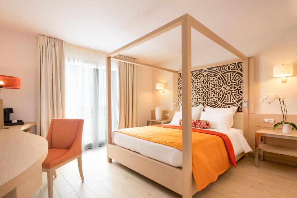Chambre de l'Akoya avec lit à baldaquin en bois clair, tête de lit décorative ethnique noire et couverture orange