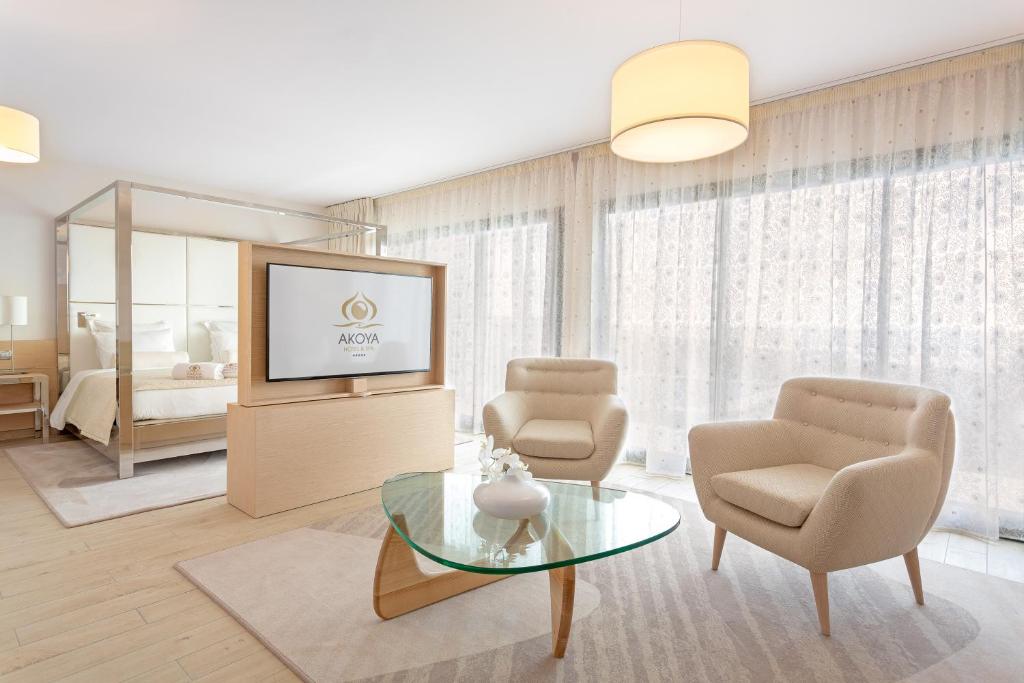 Suite de l'Akoya avec salon, fauteuils crème, table basse en verre et TV affichant le logo Akoya