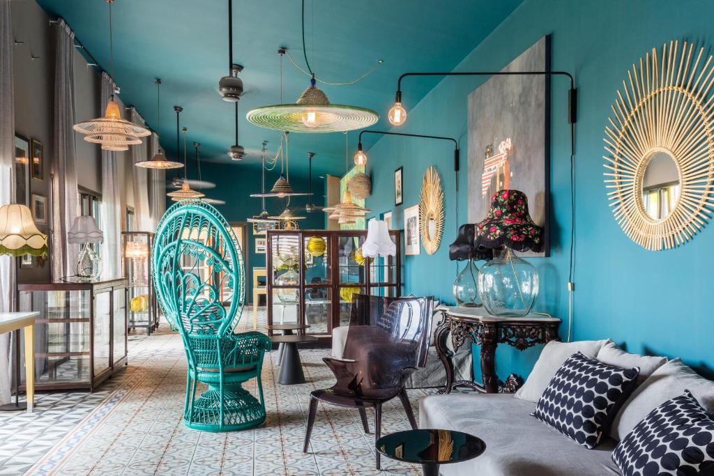 Lobby du Dina Morgabine Saint-Gilles aux murs turquoise avec fauteuil paon vert, suspensions en rotin et mobilier vintage