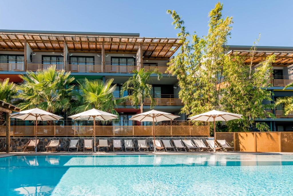 Façade et piscine du Dina Morgabine Saint-Gilles avec bâtiments modernes en bois, parasols et palmiers