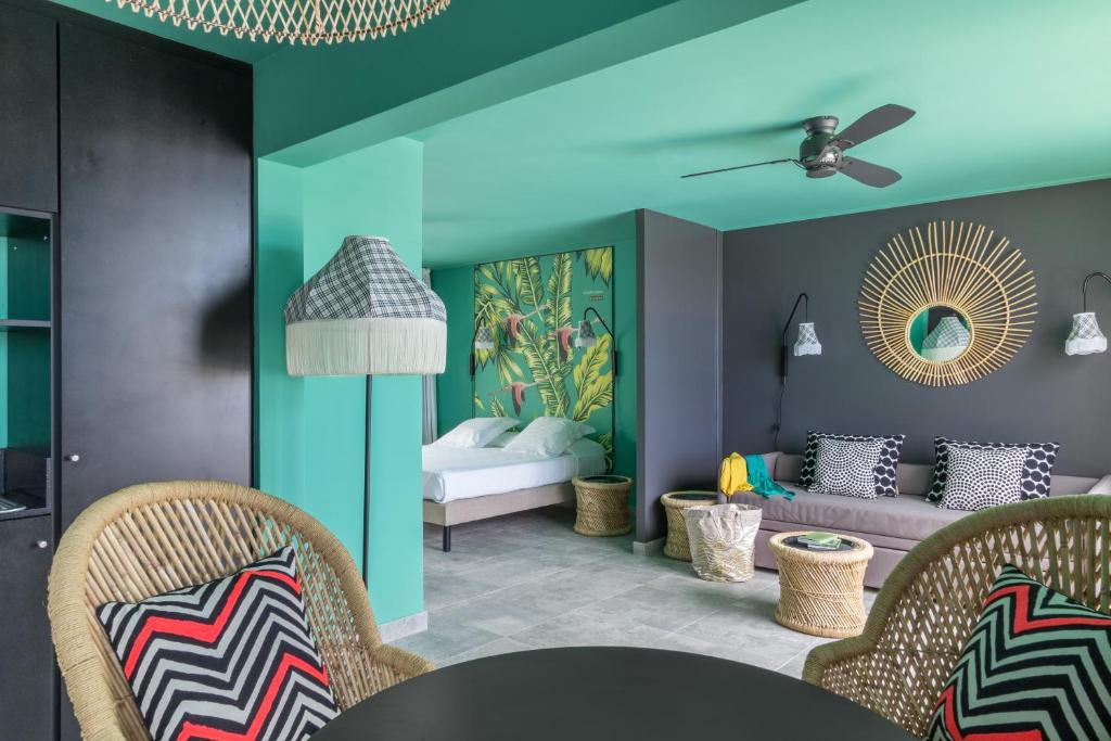 Suite du Dina Morgabine Saint-Gilles avec mur turquoise, papier peint tropical, lit double et salon avec ventilateur de plafond