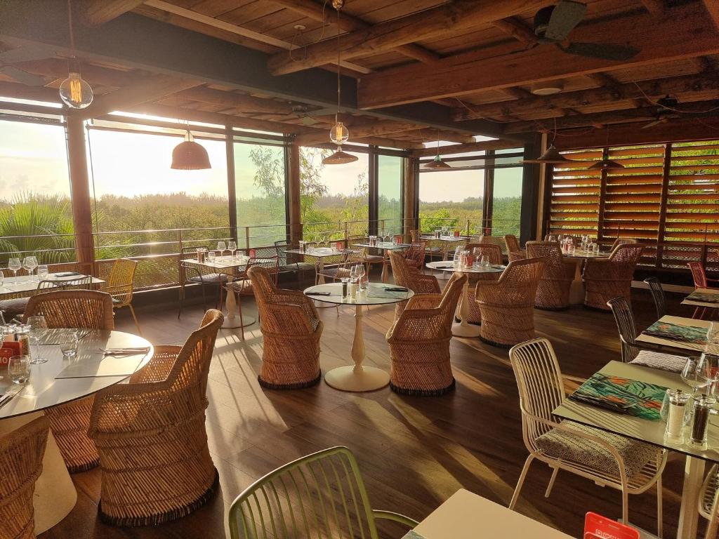 Restaurant du Dina Morgabine avec grandes baies vitrées, chaises en rotin et coucher de soleil sur la nature environnante