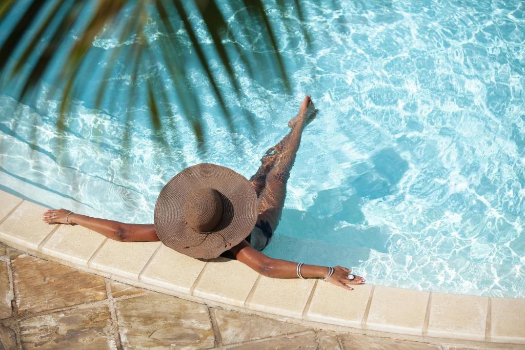Vue plongeante d'une baigneuse au chapeau de paille au bord de la piscine de l'Hôtel Le Récif sous les palmiers