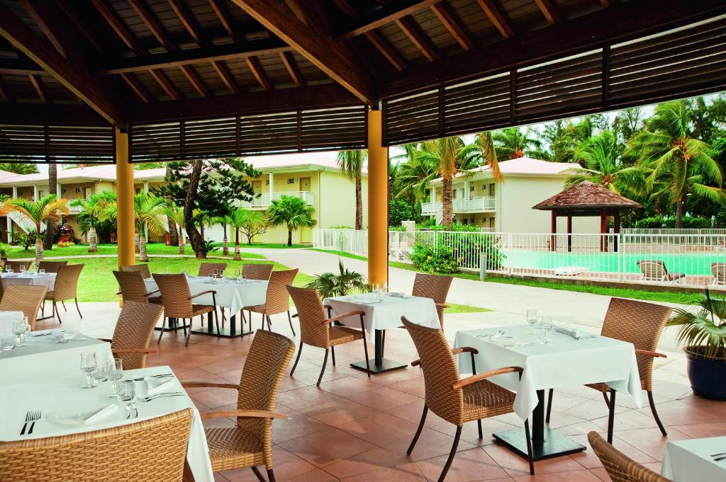 Terrasse couverte du restaurant de l'Hôtel Le Récif avec tables nappées, fauteuils en rotin et vue piscine