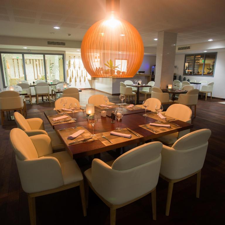 Salle du restaurant du Battant des Lames avec table dressée, chaises blanches et grande suspension orangée