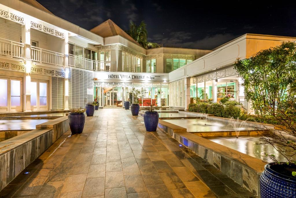 Façade de nuit de l'Hôtel Villa Delisle & Spa avec son enseigne illuminée, ses fontaines et ses jarres bleues