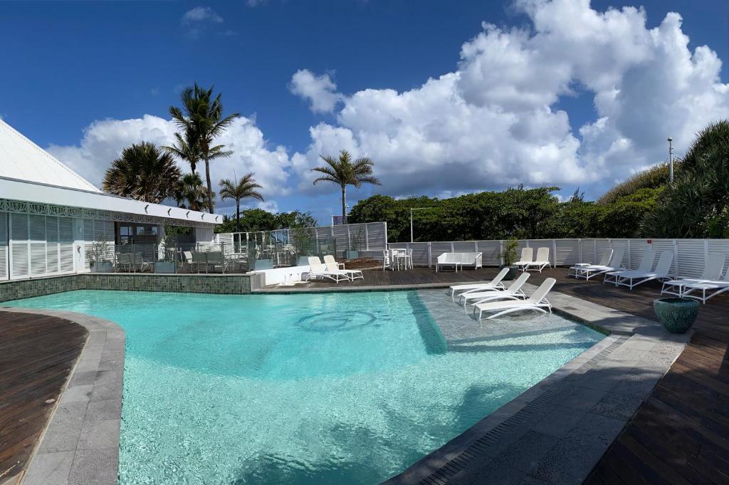 Piscine extérieure de la Villa Delisle entourée de transats blancs, avec palmiers et terrasse en bois