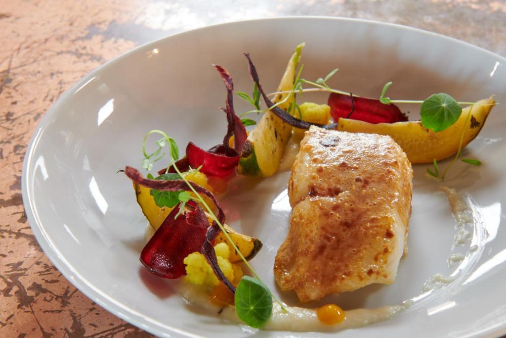 Assiette gastronomique du restaurant Dina Morgabine avec poisson rôti, légumes anciens et écume