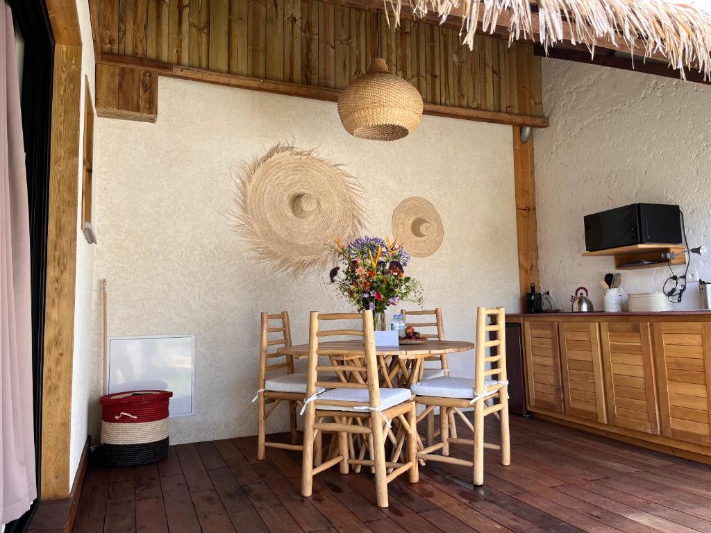 Coin repas des Vavangues avec table en bois, chaises tressées, chapeaux paille décoratifs et bouquet de fleurs sauvages