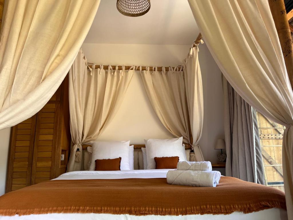 Chambre des Vavangues avec lit à baldaquin rideaux écru, coussins orange et tête de lit en bois