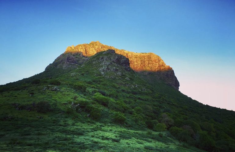 Sommet rocheux mauricien éclairé par la lumière du lever de soleil, végétation tropicale dense