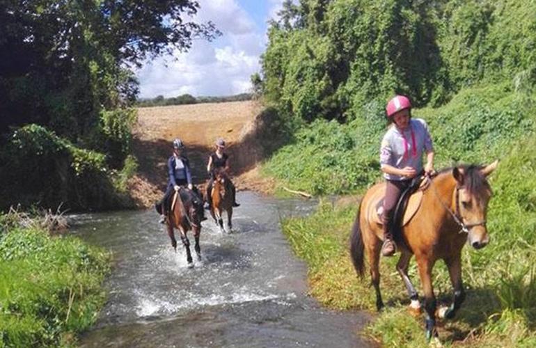Trois cavaliers traversent un cours d'eau dans la végétation tropicale, île Maurice