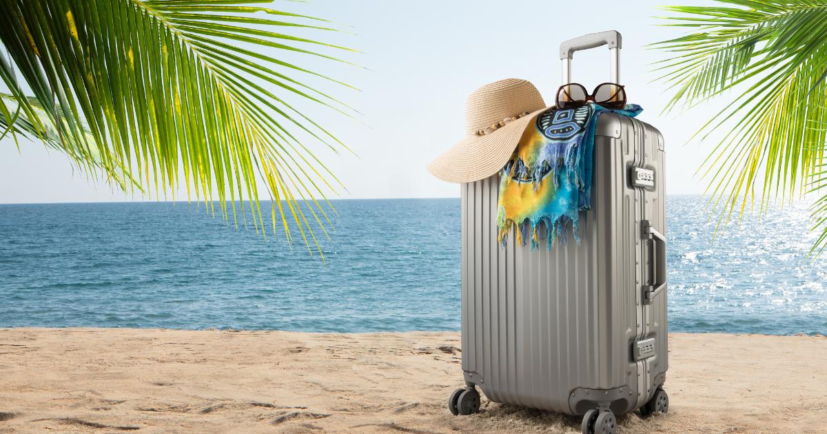 Valise grise posée sur le sable sous un palmier face à l'océan : symbole d'expatriation vers La Réunion