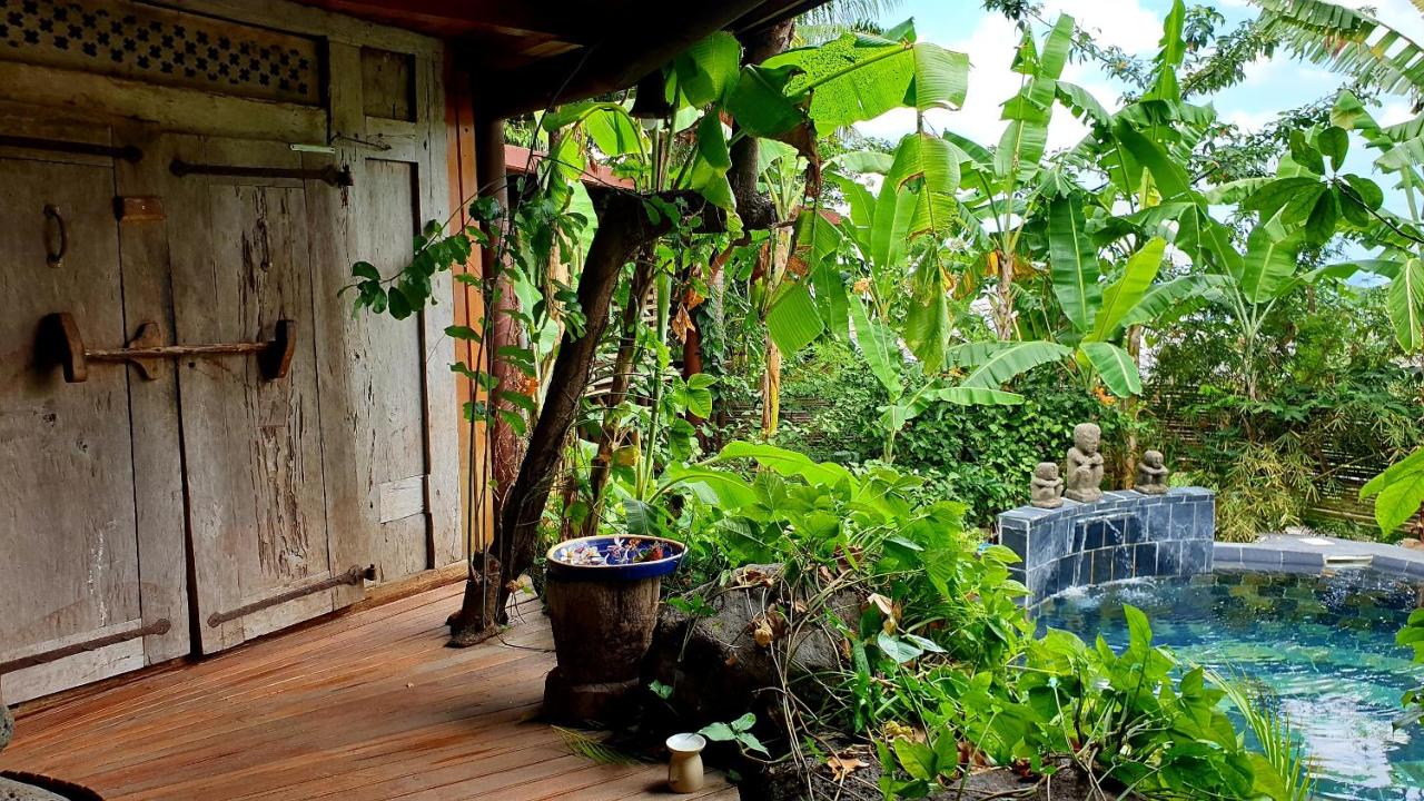 Terrasse en bois du Lodge Roche Tamarin avec porte ancienne sculptée, bananiers et bassin en pierre noire