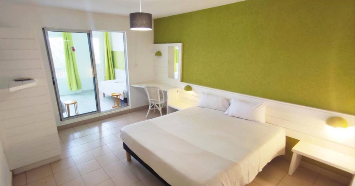 Chambre double de l'Hôtel Les Aigrettes avec mur d'accent vert anis, lit blanc et baie vitrée donnant sur la terrasse