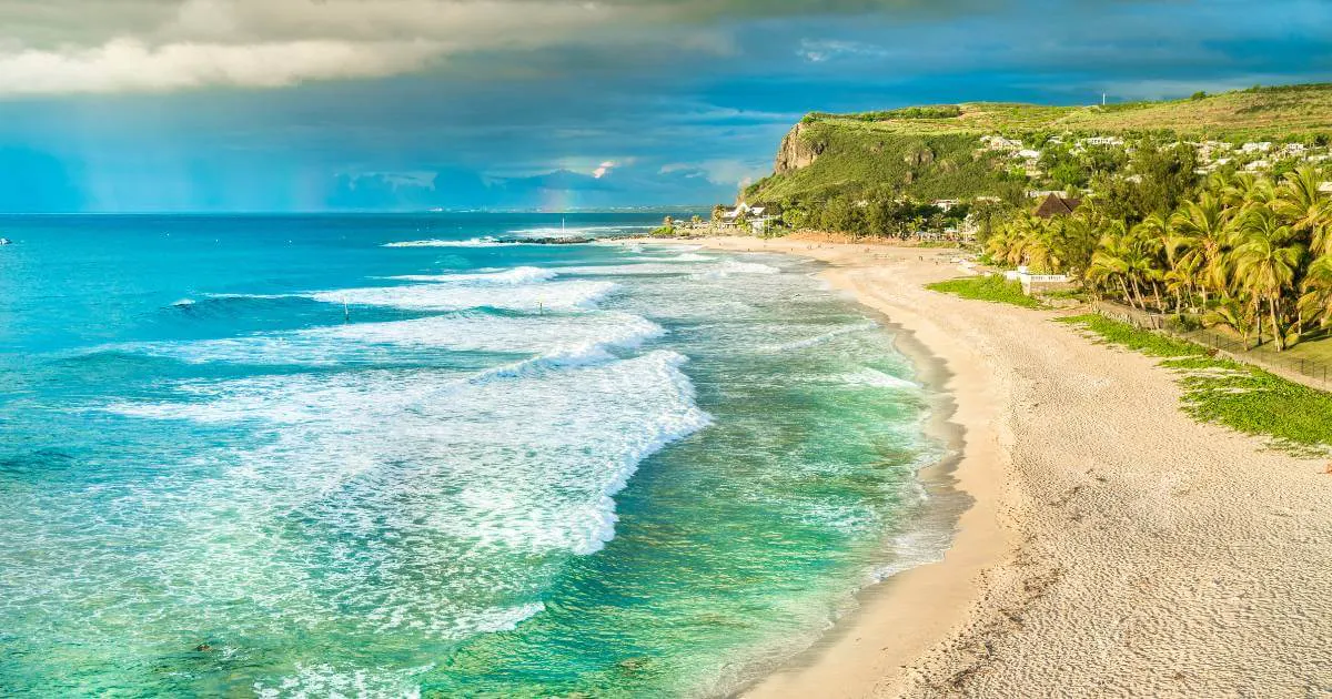 Plage de sable clair de la côte ouest de La Réunion en avril, lagon turquoise et falaise verdoyante