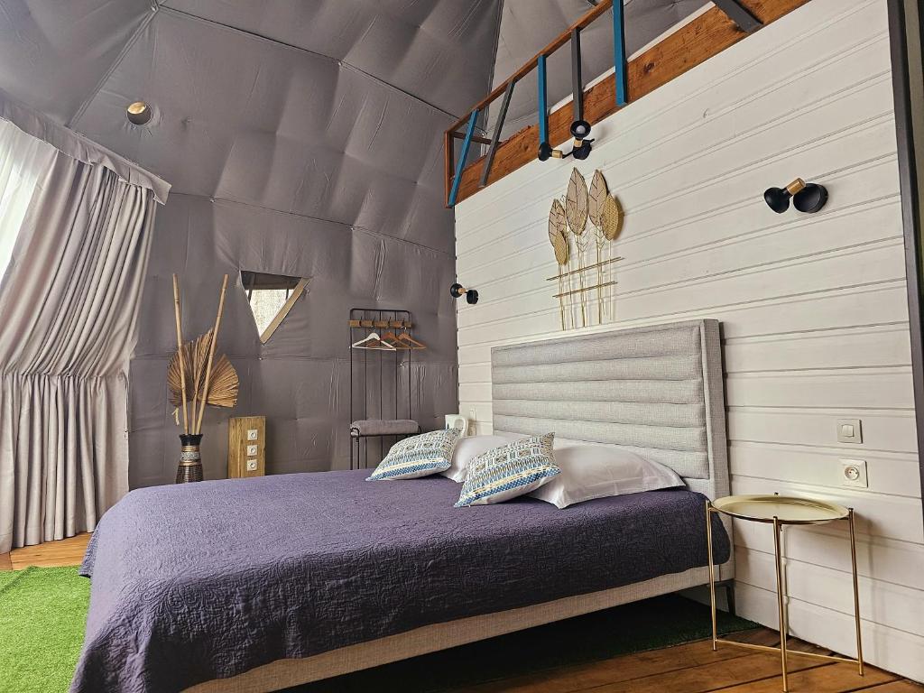 Intérieur d'un dôme : lit double avec couvre-lit violet, mur en lambris blanc et toile tendue grise au plafond
