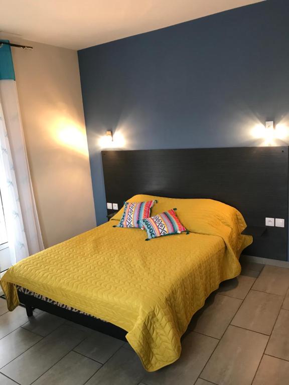 Chambre du gîte Le Guétali avec lit double, couvre-lit jaune, tête de lit sombre et mur d'accent bleu