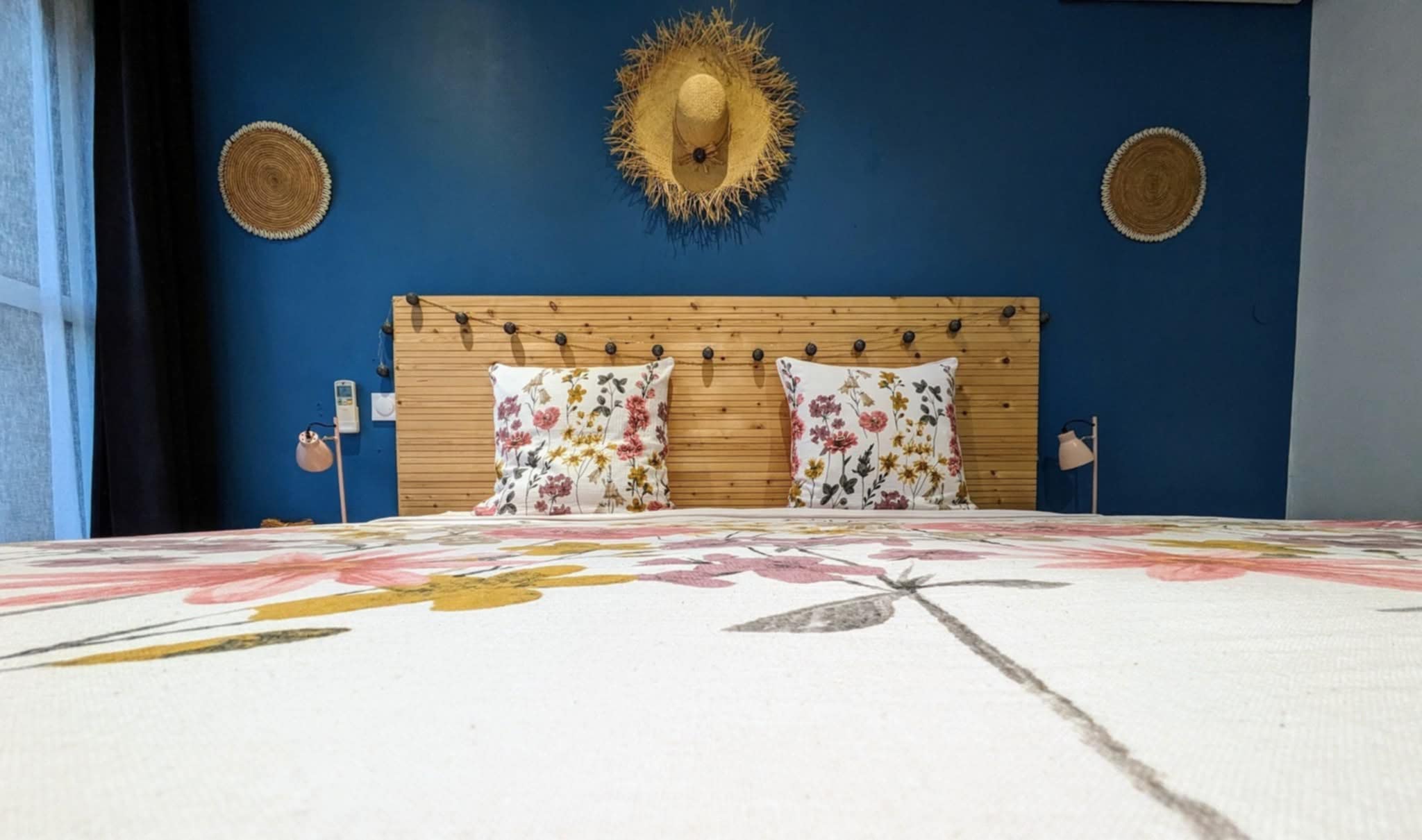 Intérieur d'une chambre double à Eskal Péi, tête de lit bois, parure florale, mur bleu marine