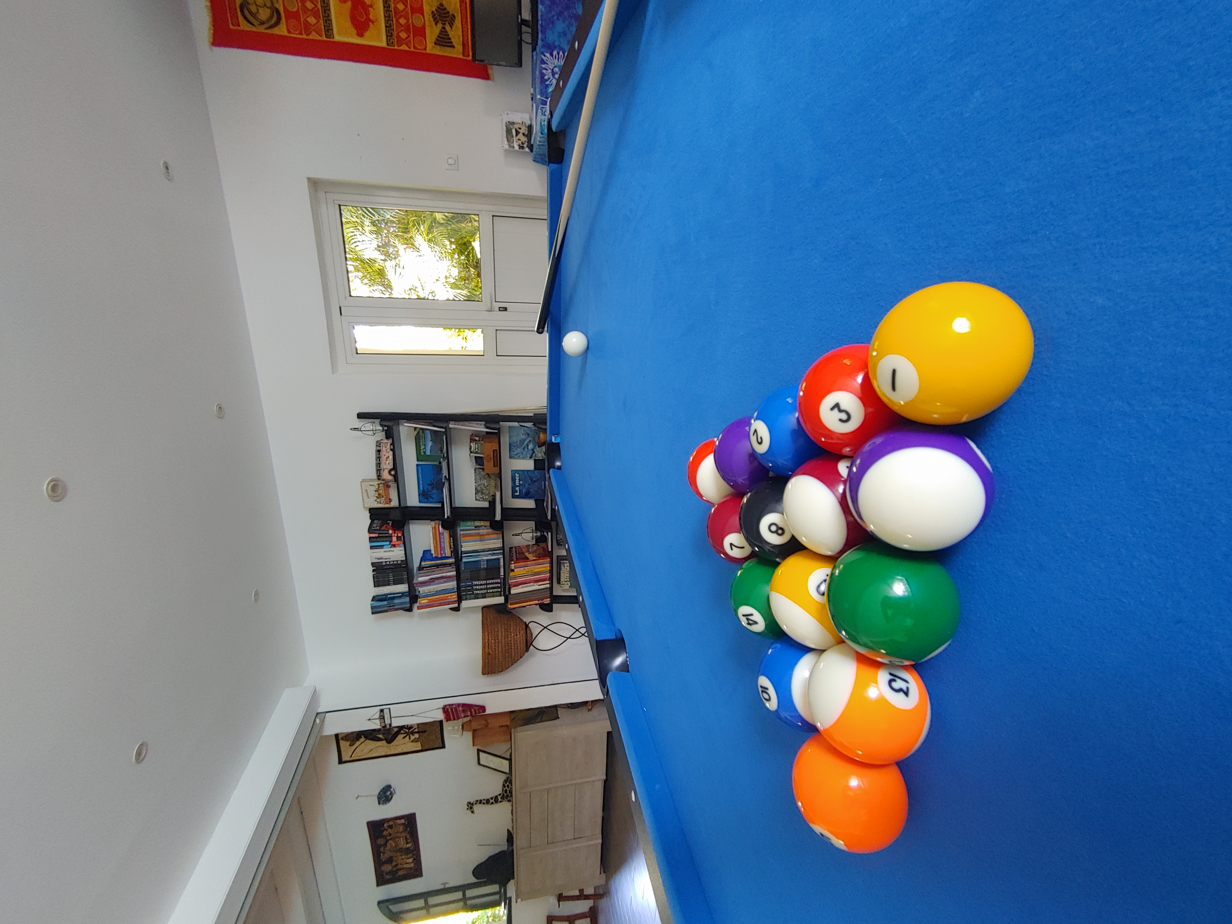Billard bleu d'Eskal Péi avec boules en triangle et bibliothèque en arrière-plan