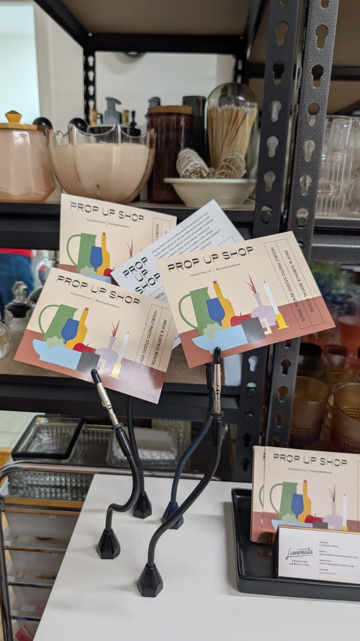 Prop Up Shop business cards propped against ceramics on a metal prop-house shelf