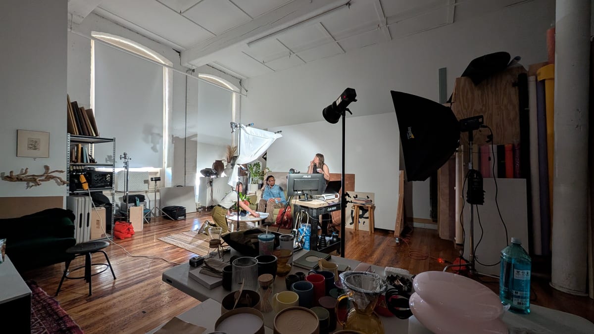 Wide view of a lit photo set with tables of props, buckets and ceramics piled just outside the camera's view