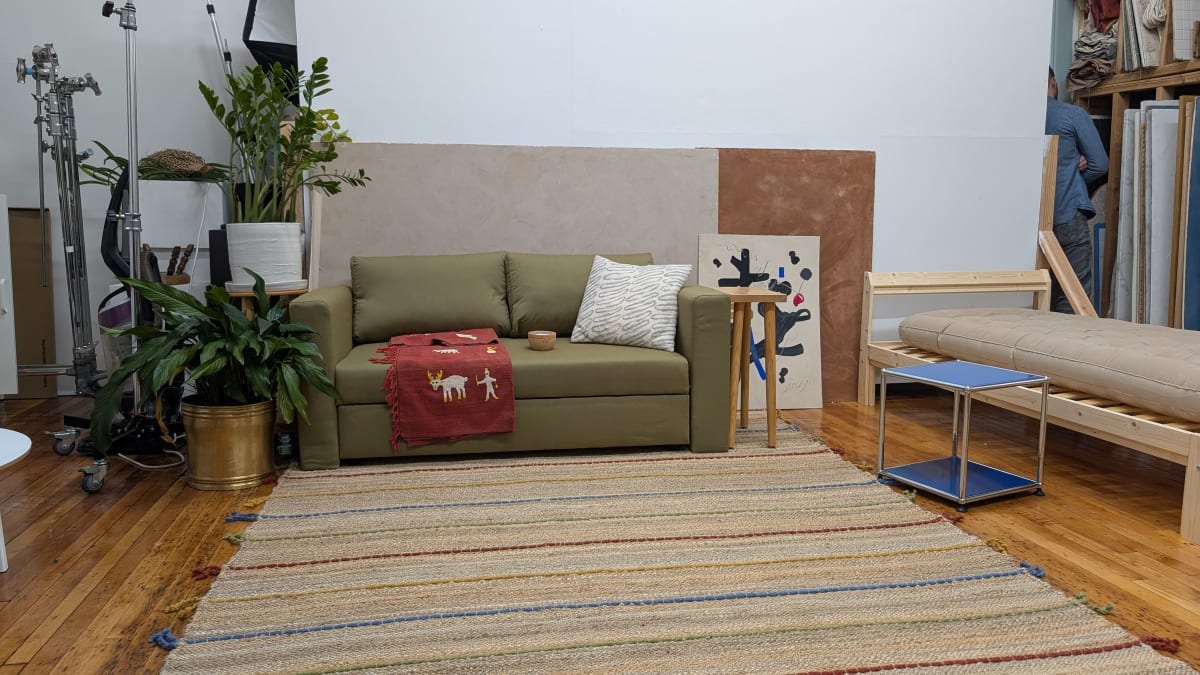 A living room set assembled inside a photo studio, with lighting stands and storage shelves visible at the edges of the frame