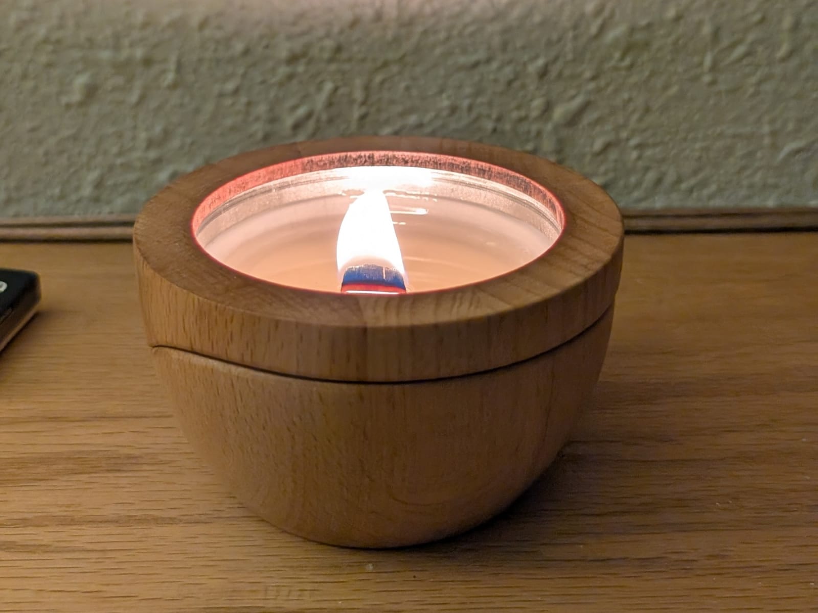 A Sero candle in its beech wood container, mid-burn, with a steady flame and a fully formed melt pool.
