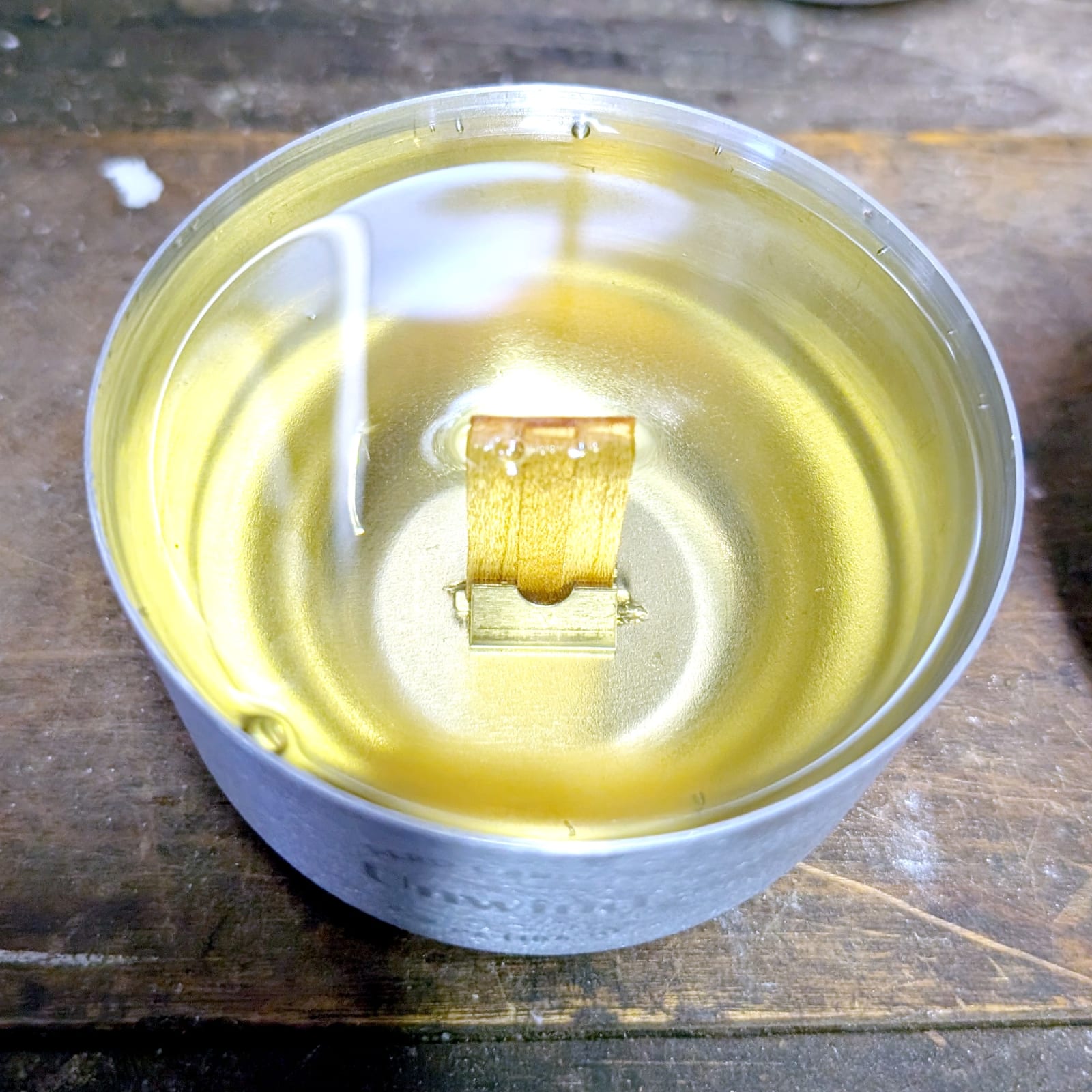 Close-up of a Sero aluminum candle insert showing the welded wick clip at the base of the cup, holding the wood wick upright in a pool of liquid wax.