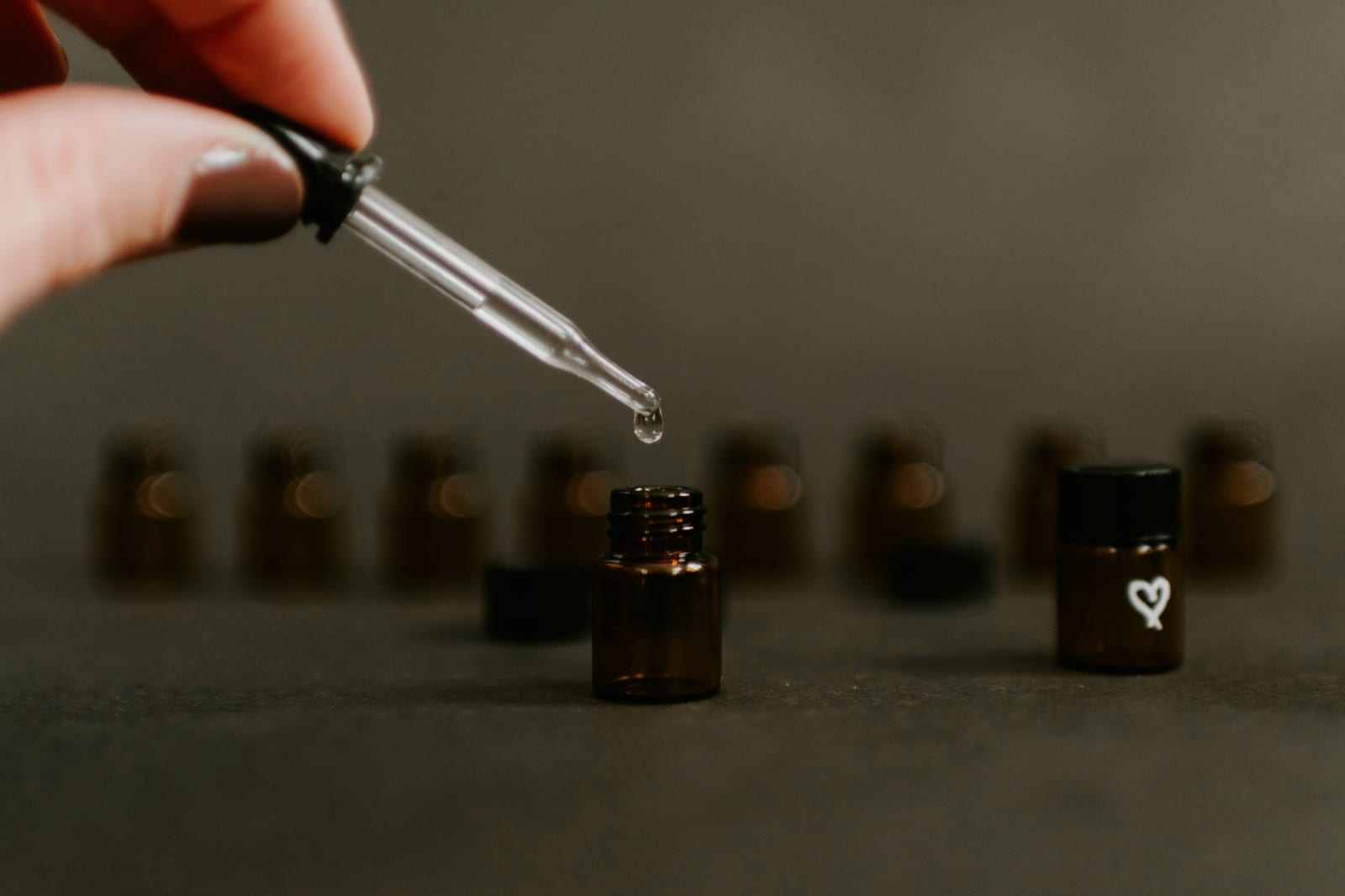 A hand using a glass dropper to evaluate amber-bottled fragrance compounds during scent testing.