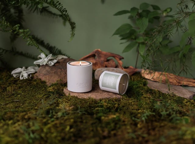 A Grow Fragrance candle lit in its reusable vessel with a second aluminum insert lying beside it.