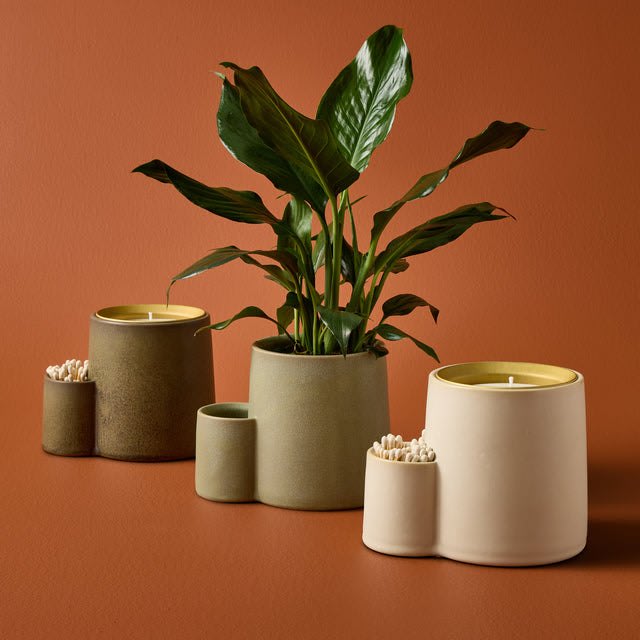 Modern Sprout Ember Earth ceramic vessels, one planted with a leafy houseplant and others holding candles and matches.