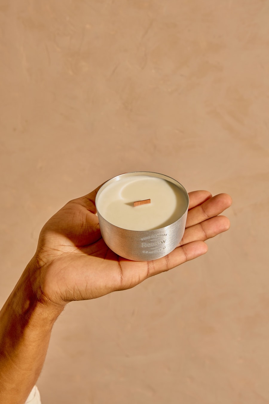 An open palm holding a lit aluminum Sero candle against a warm terracotta plaster wall