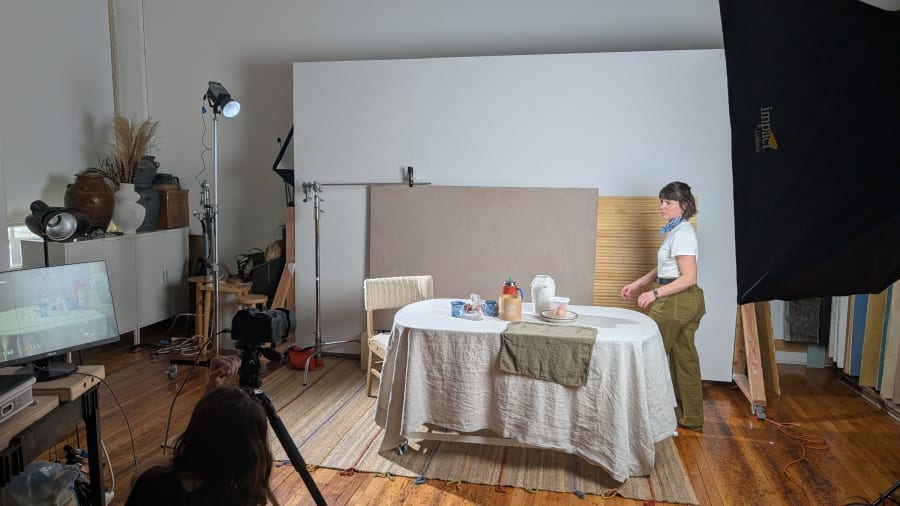 A round folding table draped in linen being styled inside a studio, with lighting stands and a monitor nearby
